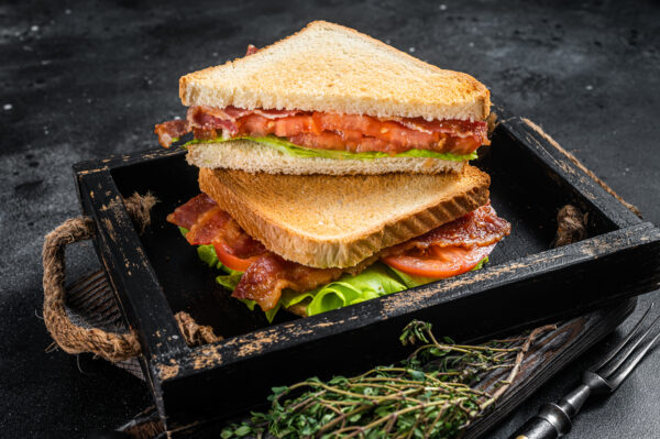 Homemade toasted BLT sandwich with bacon, tomato and lettuce in wooden tray.